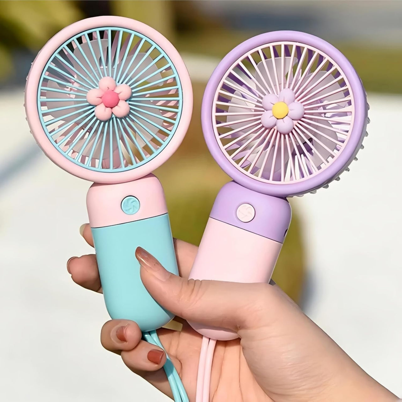 Two handheld fans, one pink and blue, the other purple and white, held by a hand against a blurred background.