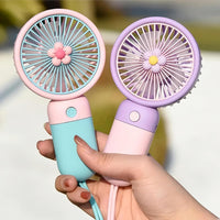 Two handheld fans, one pink and blue, the other purple and white, held by a hand against a blurred background.