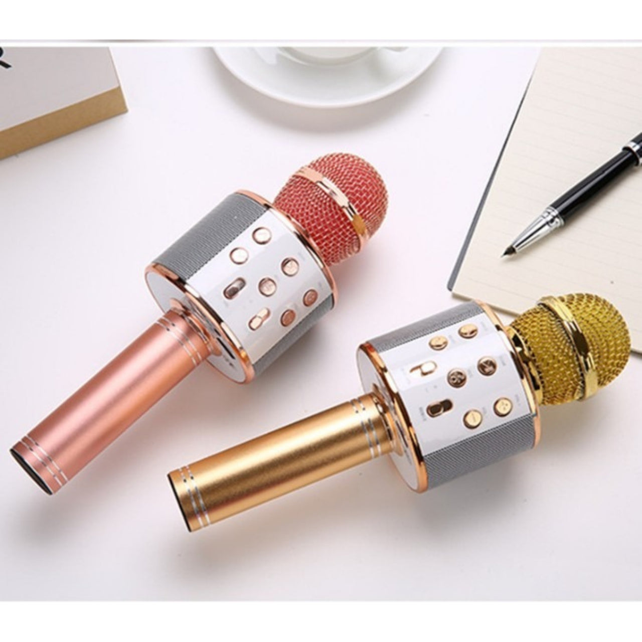 Two metallic microphones on a white surface with a notebook and pen in the background.